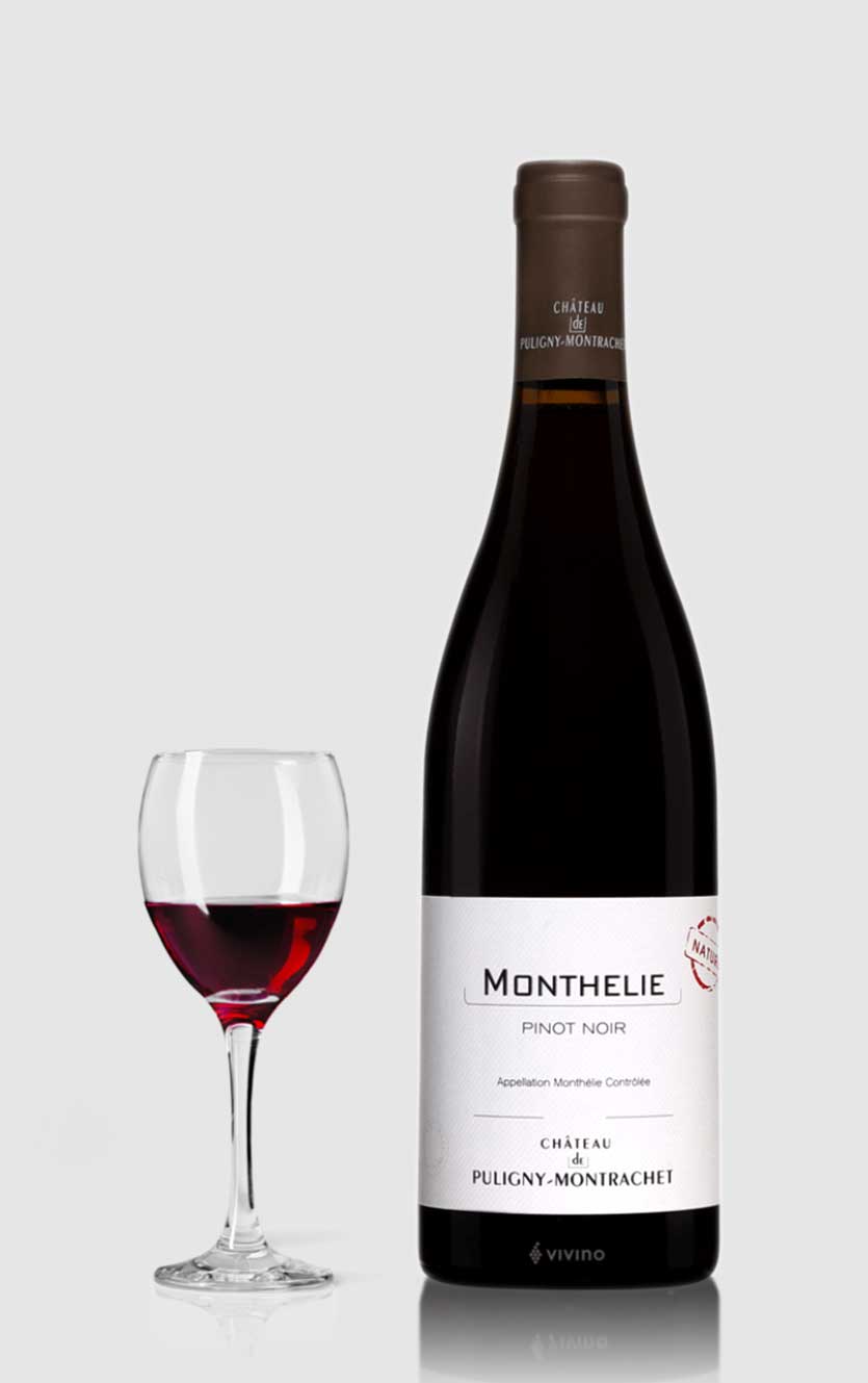 En flot flaske Château de Puligny-Montrachet Monthelie Rouge Nature 2016 biodynamisk rødvin fra Bourgogne serveret ved siden af et glas rødvin