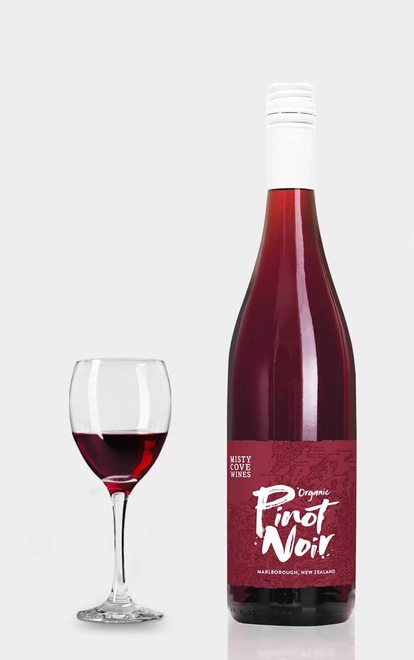 En flot flaske Misty Cove Pinot Noir økologisk rødvin fra New Zealands Marlborough-region serveret ved siden af et glas rødvin på et bord