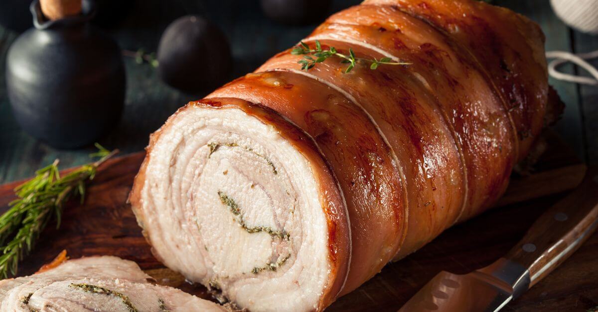 En hel, saftig porchetta med perfekt sprøde, boblende svær, der hviler i kurven på en moderne airfryer. Stegen er gyldenbrun, og man kan se krydderurterne titte frem i enderne.