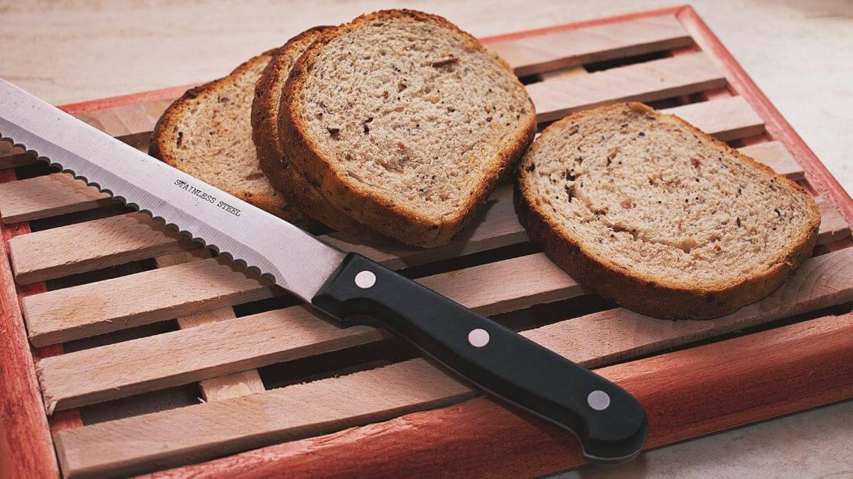 Hjemmebagt Kneippbrød fra airfryer skåret i skiver på træskærebræt med brødkniv – sundt fuldkornsbrød med kerner