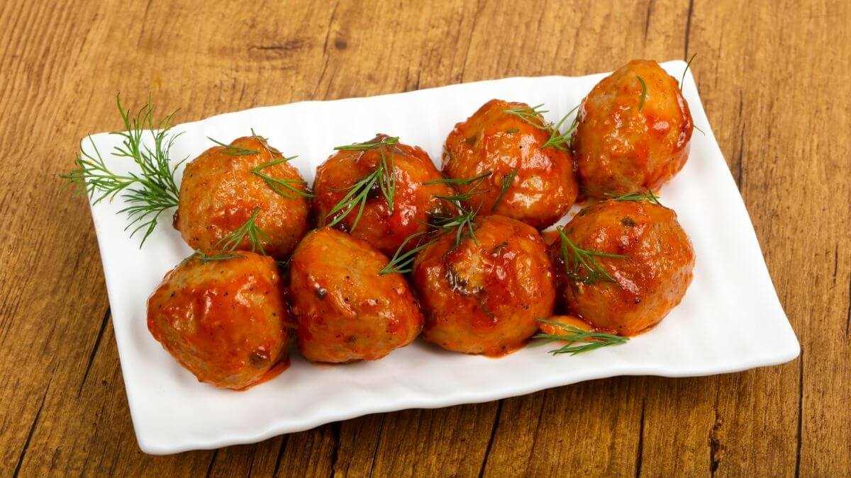 Kinesiske kyllingefrikadeller i airfryer serveret med blank glaze på et aflangt hvidt fad som nem asiatisk aftensmad