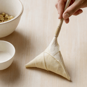 En samosa, der foldes i trekanter og lukkes med melklister