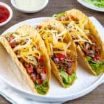 Tacoskaller fyldt med hakket oksekød, ost, hakkede løg, fintskåret tomater og agurker og majs fra dåse med salat i bunden.